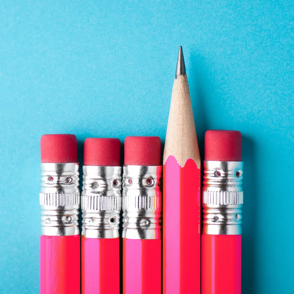 Een rij roze potloden, waarvan er één als enige is geslepen